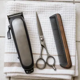 A close view of hair clippers, scissors and a comb resting on a folded towel