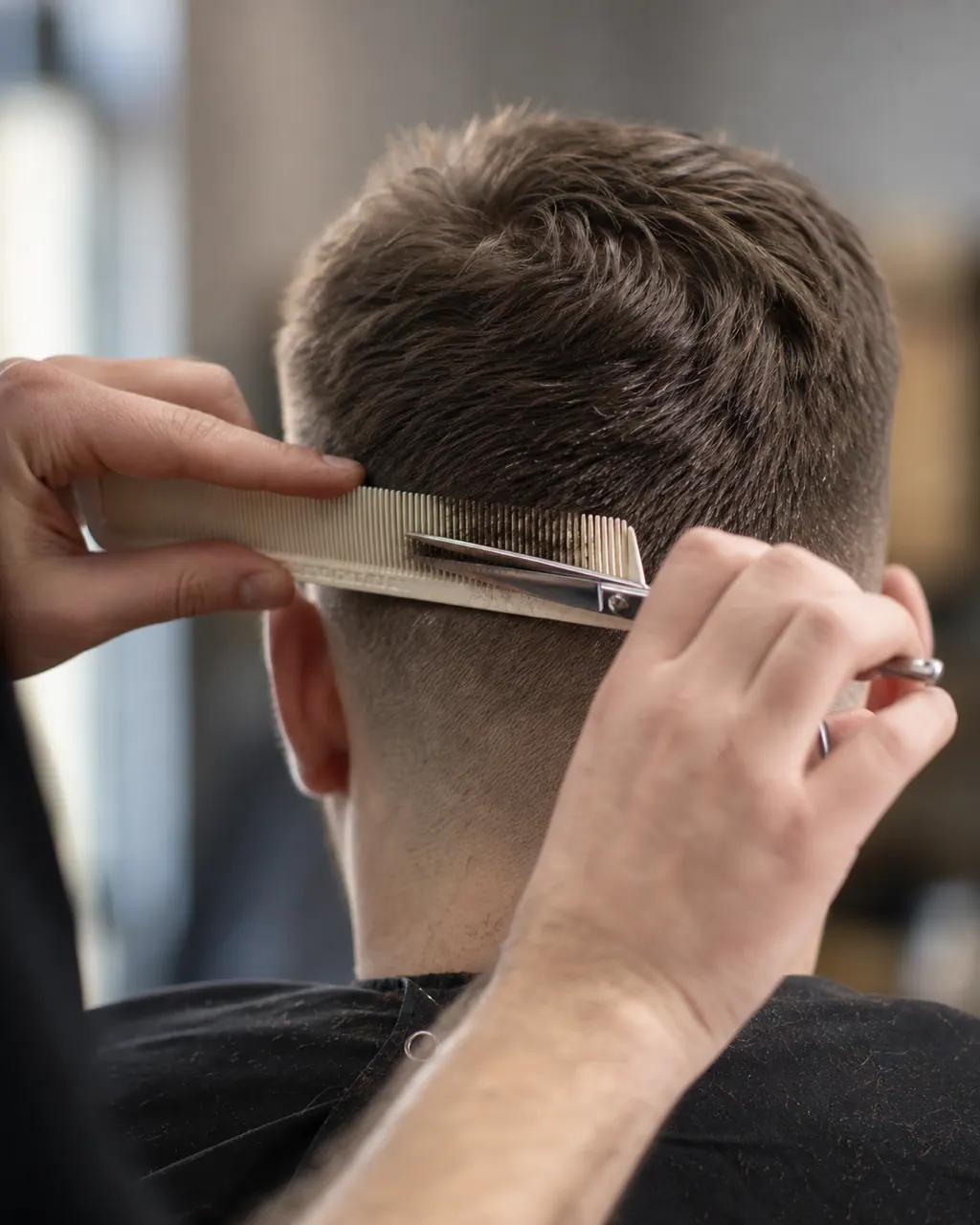 A barber's hands guiding scissors and comb through the back of a short haircut